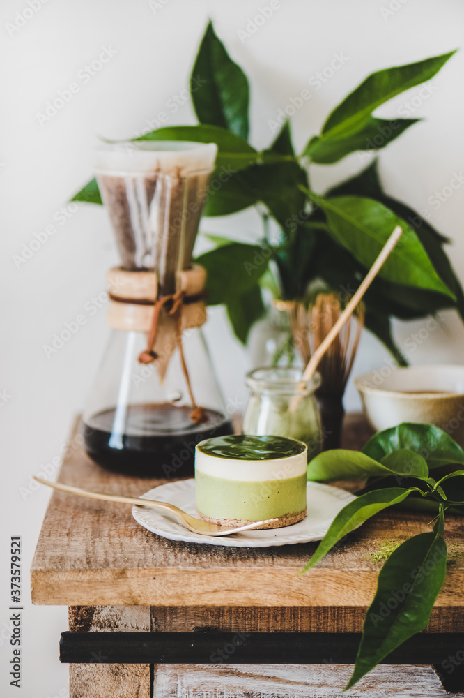 咖啡和甜点设置。绿色抹茶芝士蛋糕和煮好的倒在木头上的玻璃烧瓶里的咖啡