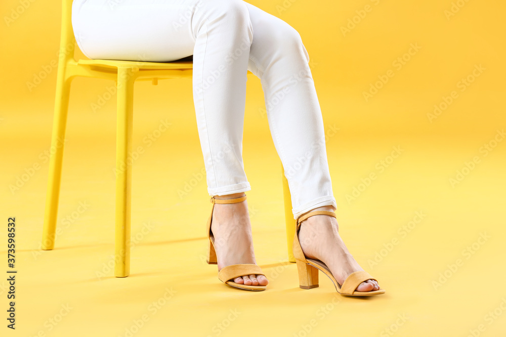 穿着时尚鞋子坐在彩色背景下的椅子上的年轻女性