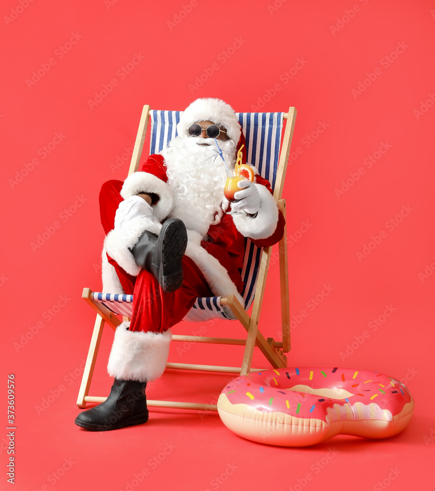 非洲裔美国圣诞老人，在彩色背景下，拿着鸡尾酒坐在躺椅上