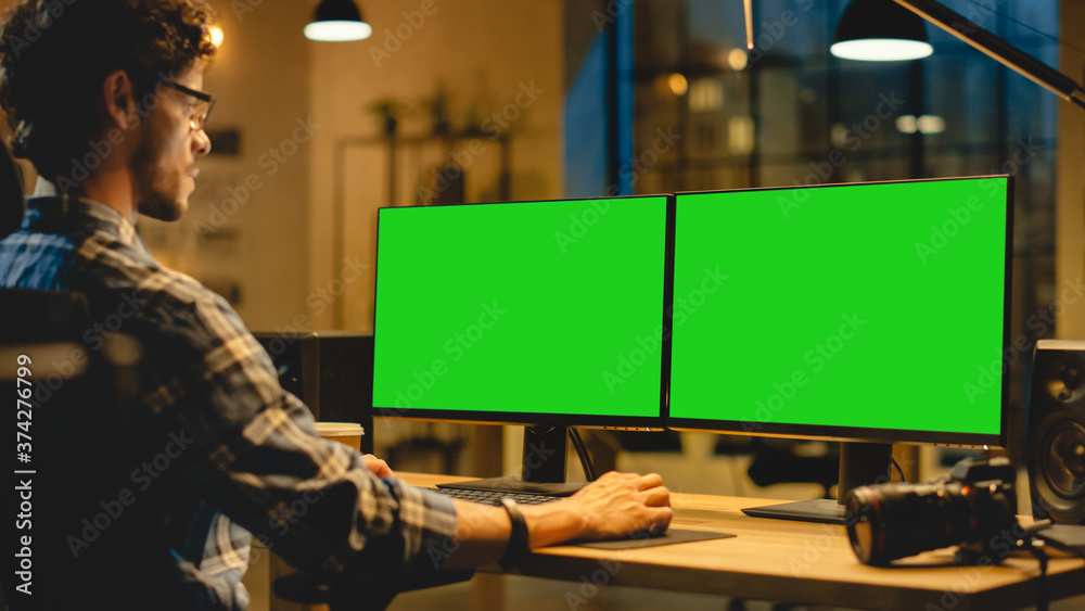过度：创意设计师坐在桌子旁使用带有两个绿色实体u的台式电脑