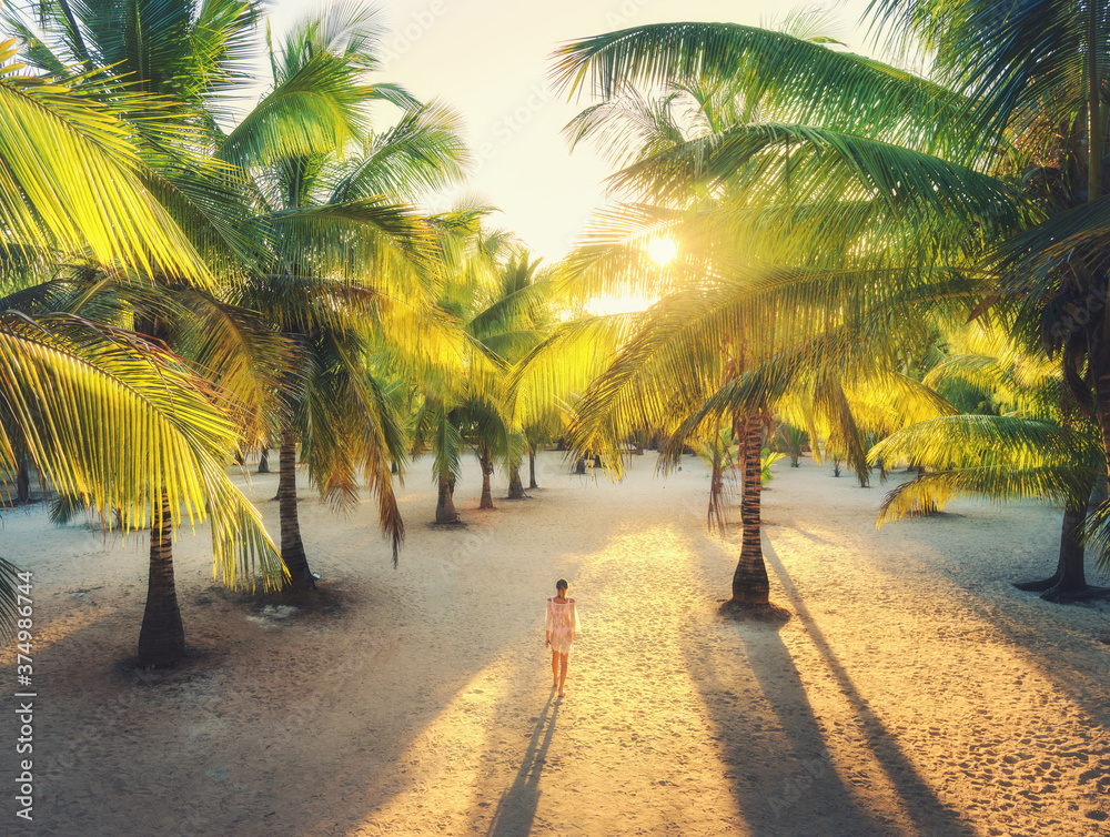 美丽的年轻女子在日落时走在棕榈巷子里。夏季旅行。带sli的热带景观