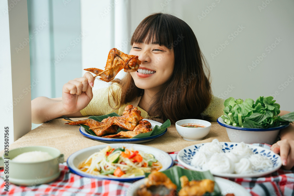 年轻亚洲女性喜欢吃烤鸡翅棒的画像。