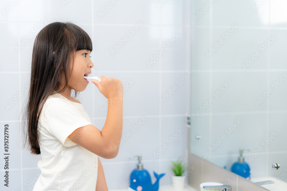 可爱的亚洲小学女孩在家里的浴室里刷牙照镜子。早上