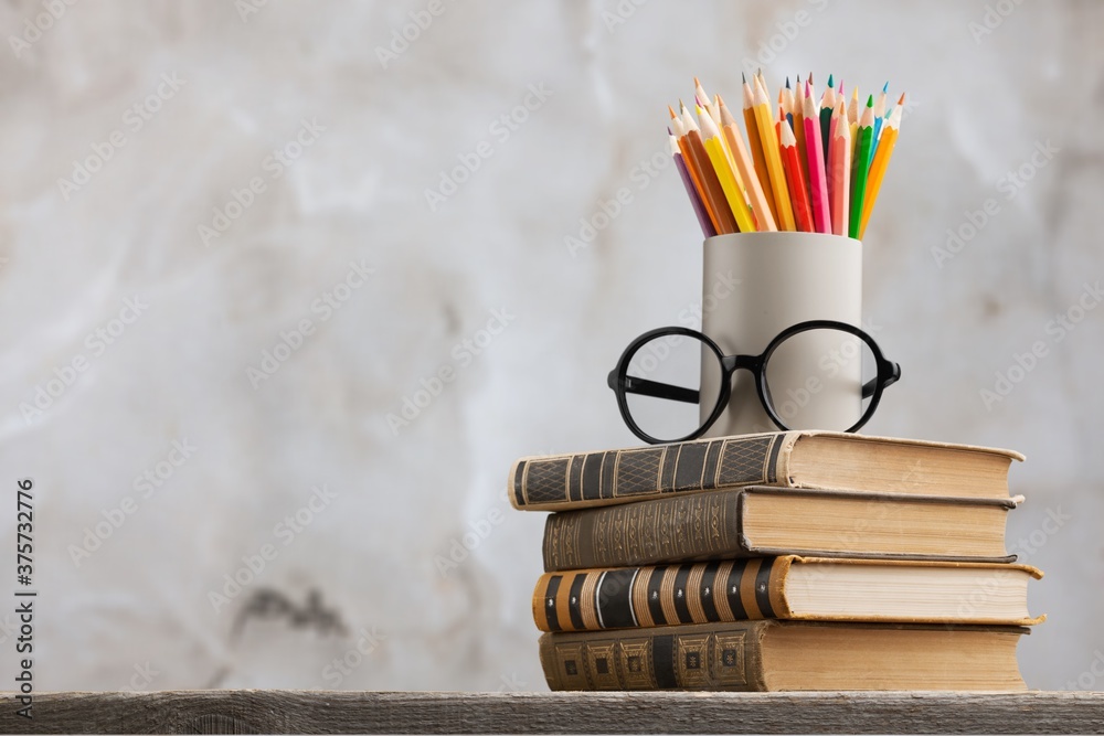 A stack of books with glasses and pencils on the desk