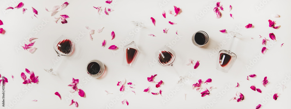 装在玻璃杯里的红酒。平坦的酒杯，白底上有红酒和粉红色的花瓣