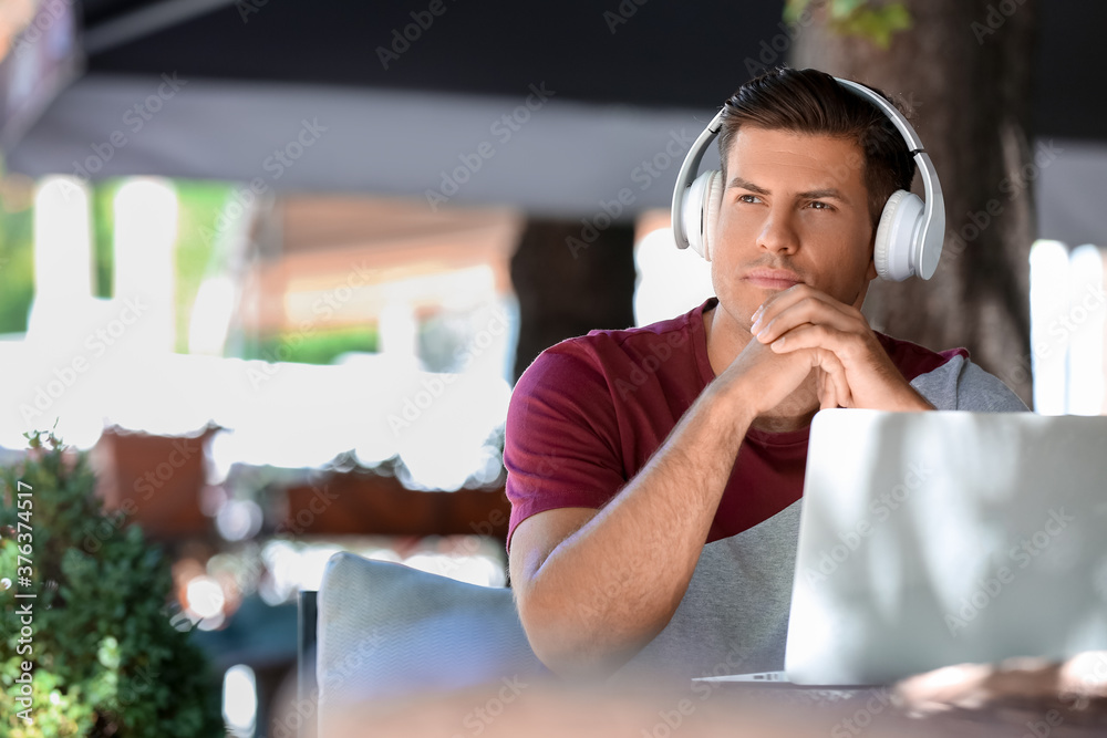 戴着耳机的男子在户外咖啡馆用笔记本电脑工作
