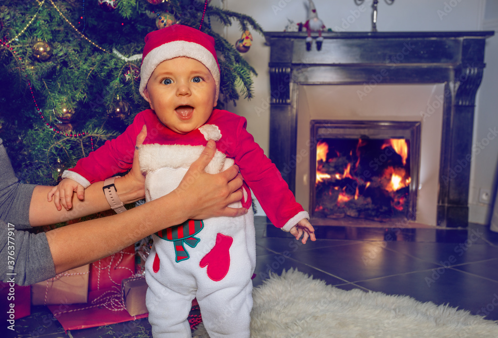 快乐的蹒跚学步的小男孩在圣诞树前，妈妈们手里拿着壁炉