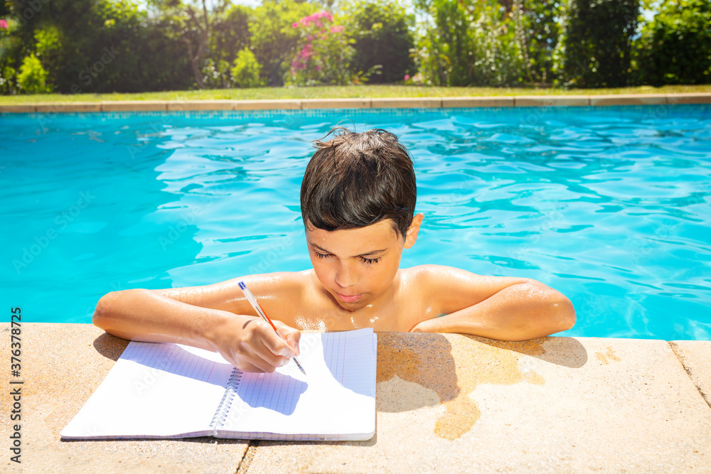 游泳池里做作业的小男孩在边上拿着笔微笑着看课本