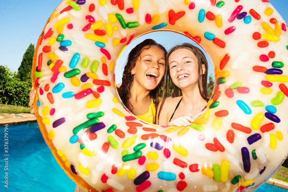 两个朋友，年轻女孩，拿着充气浮标甜甜圈站在游泳池的边界上