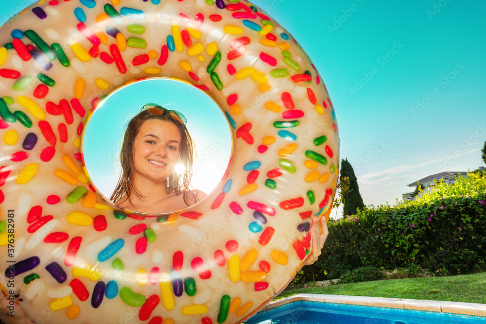 Cute teen girl stand together with inflatable buoy doughnut on the border of swimming pool smiling o