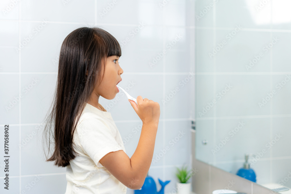 可爱的亚洲小学女孩在家里的浴室里刷牙照镜子。第二天早上