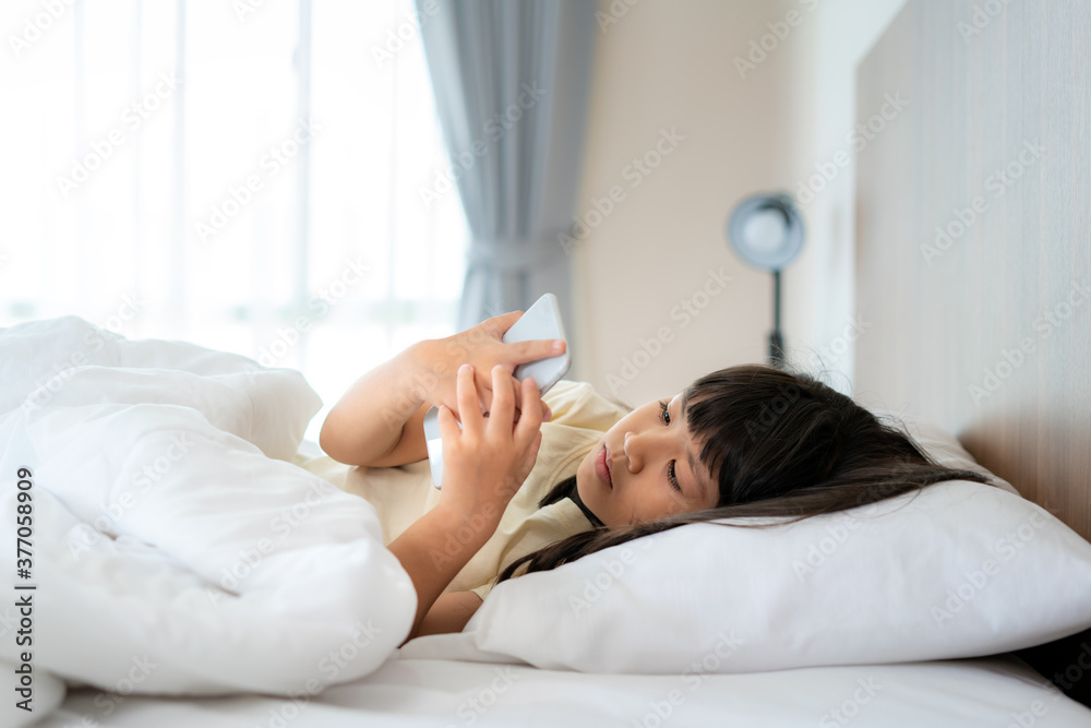 快乐的亚洲女孩，早上躺在家里卧室的床上看手机