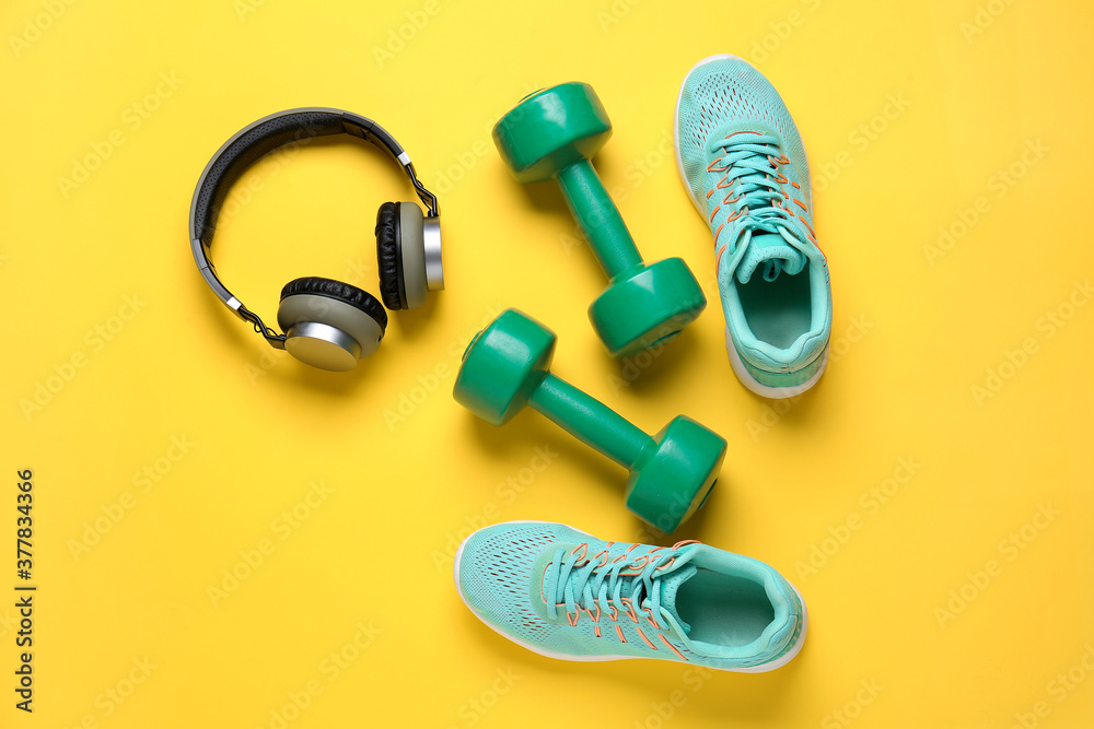 Sportive shoes, dumbbells and headphones on color background