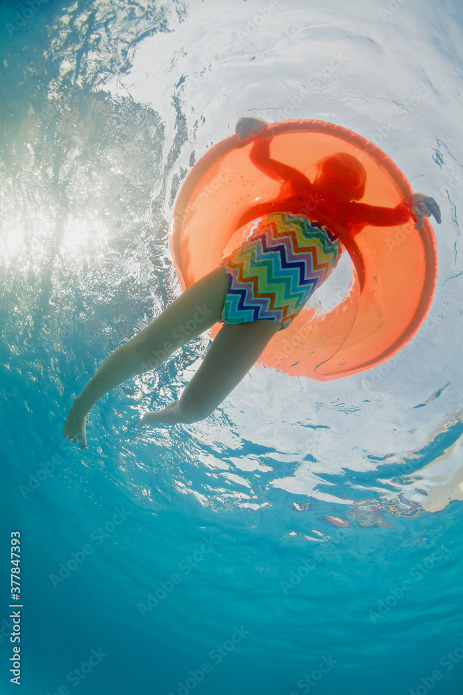 有趣的水下照片，小女孩在水上公园或beac的橙色充气管上有趣地游泳