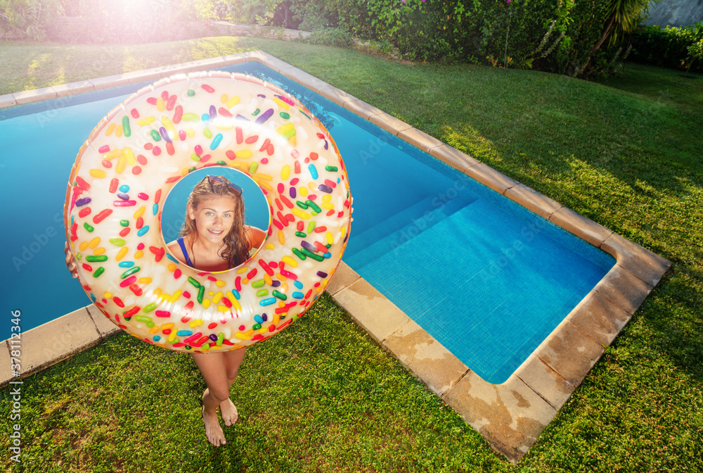 Happy smiling teen girl stand with inflatable buoy doughnut on the border of swimming pool view from