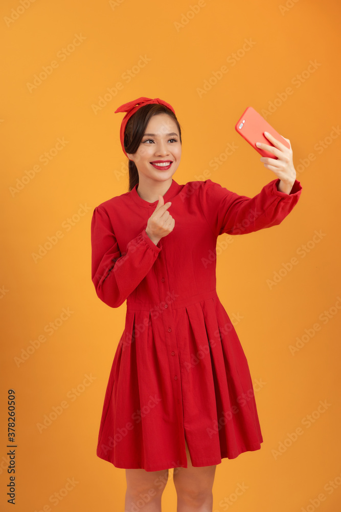 Shot of a happy young Asia woman taking selfie with her cellphone while standing isolated over orang