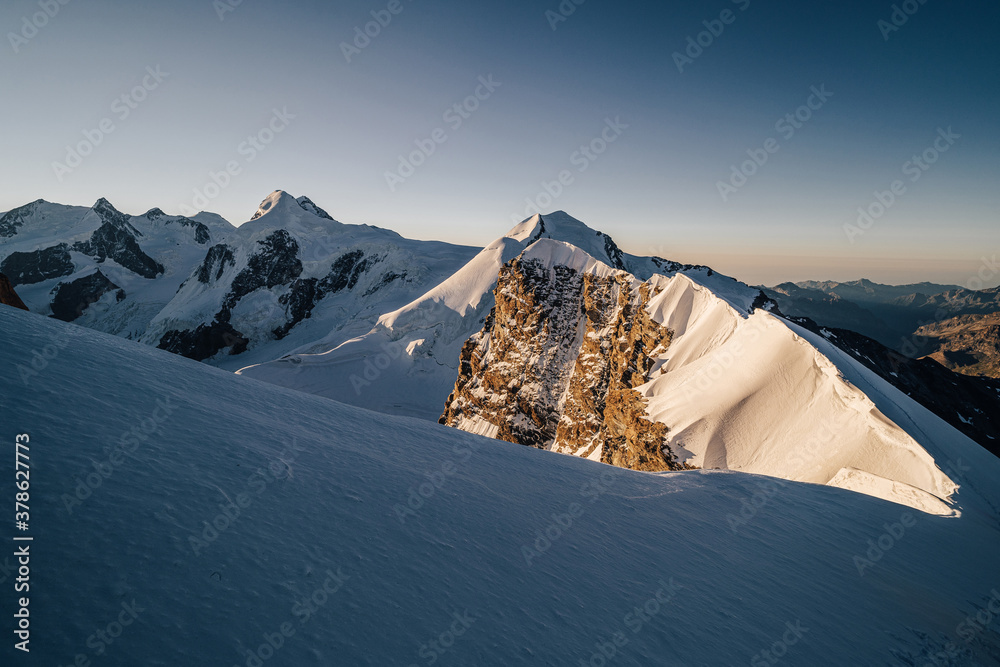 Beautiful alpine mountain landscape during sunrise or sunset. Snow ridge with rocks and cornices, su