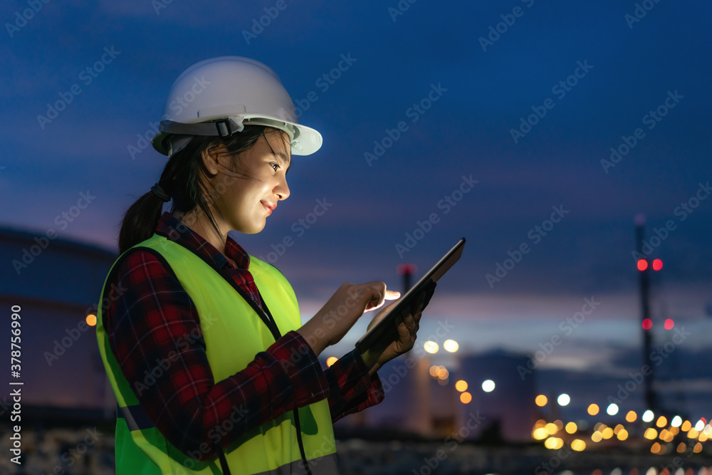 Asian woman petrochemical engineer working at night with digital tablet Inside oil and gas refinery 