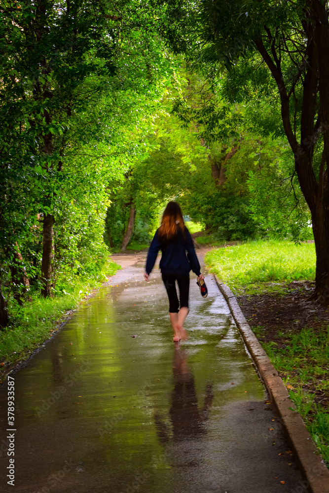 A girl walks barefoot along an alley in the pouring rain.