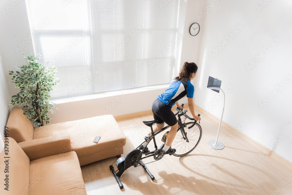 亚洲女自行车手。她在家锻炼。在教练机上骑自行车，玩网上自行车ga
