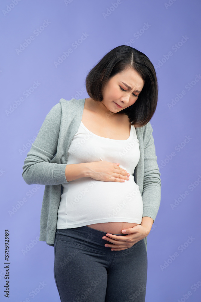 孕妇腹部疼痛，站在淡紫色背景上触摸腹部