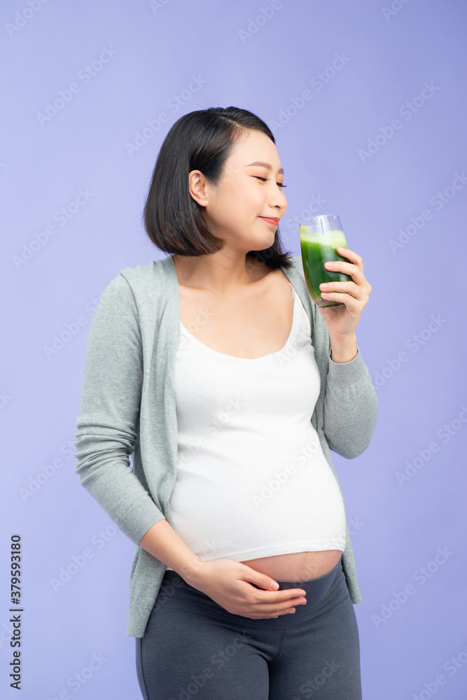 Happy pregnant asian woman drinking green vegetable juice or smoothie at home