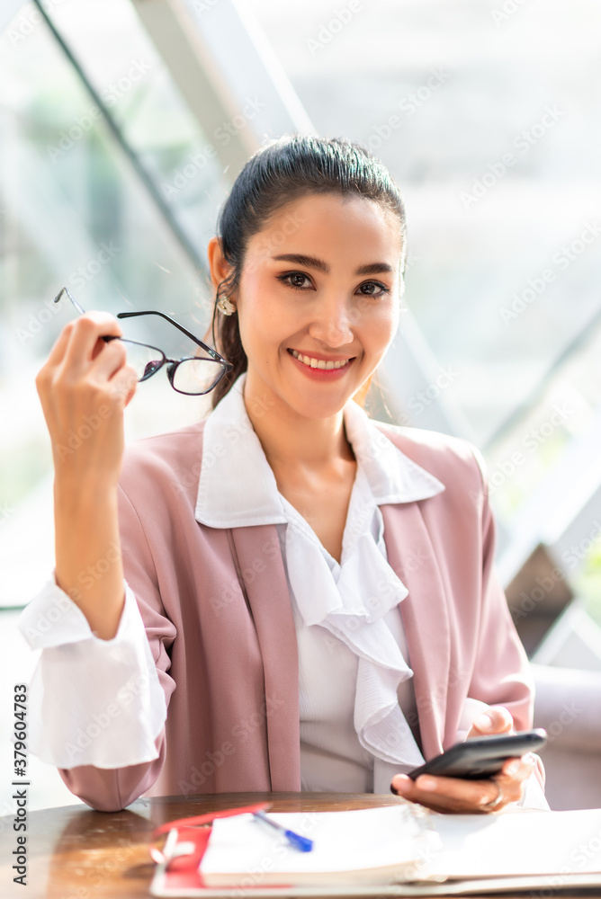 Business woman in pink suit smile and working on smartphone in the morning hold eye glasses