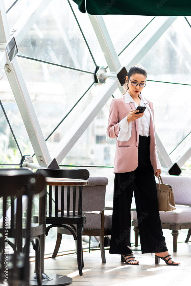 Business woman in pink suit standing and use smartphone in the morning in cafe