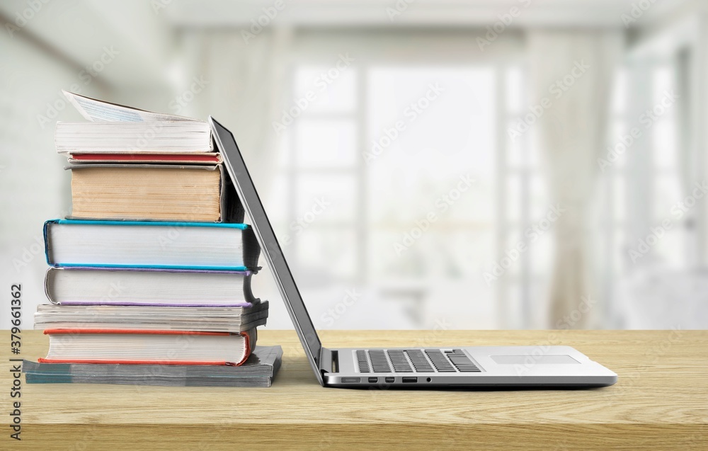 Stack of books with modern laptop on table