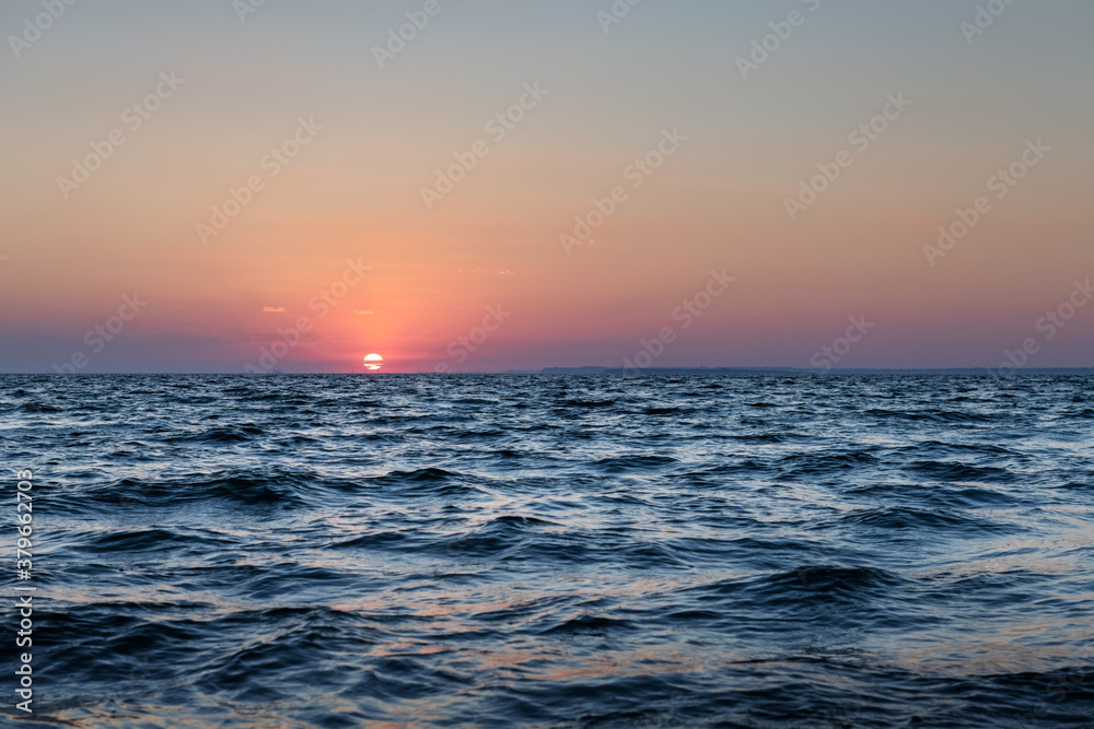 Sunset in the ocean with large sun dusk soft waves and red cloudy sky. Sea sunrise background. Lands