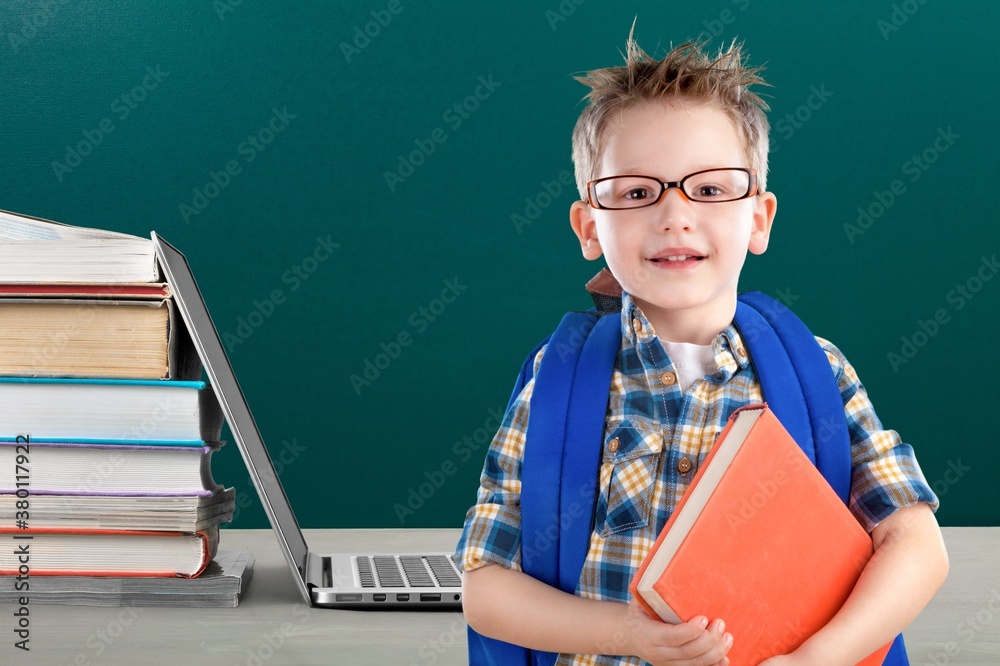 Stack of books with laptop on table and cute school boy