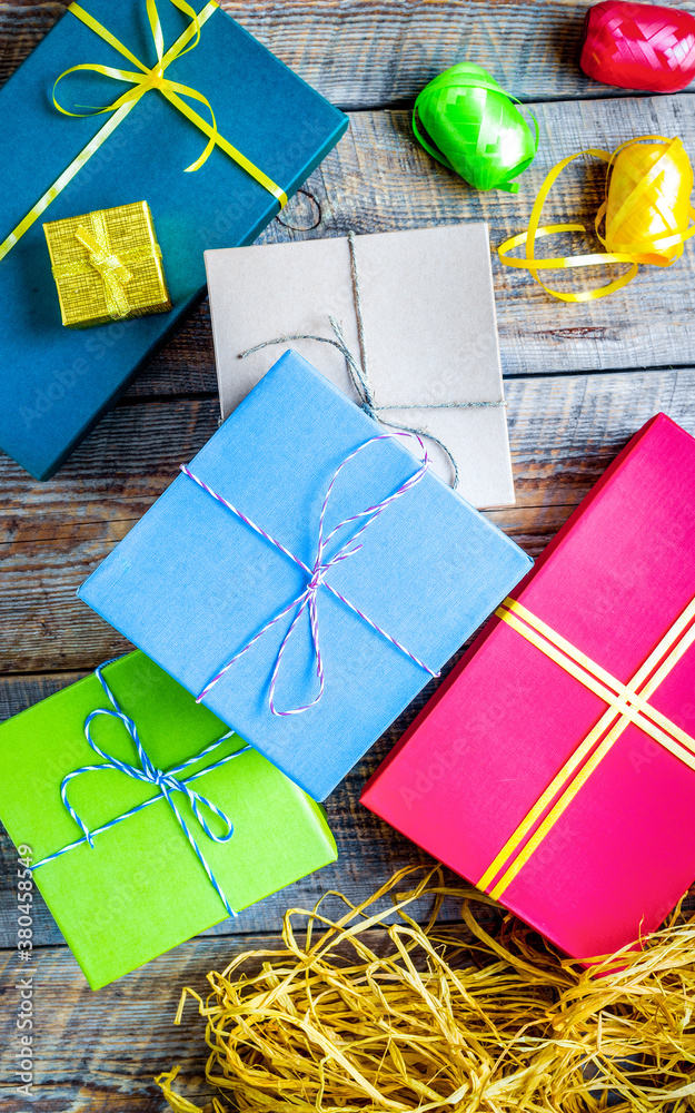 Colored gift boxes on wooden background with ribbon and straw