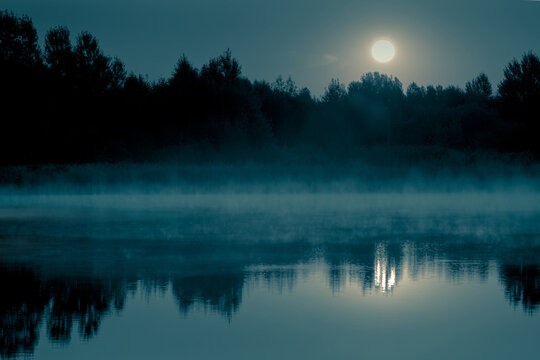 夜晚神秘的风景。满雾的河上的满月和它在静水中的倒影。