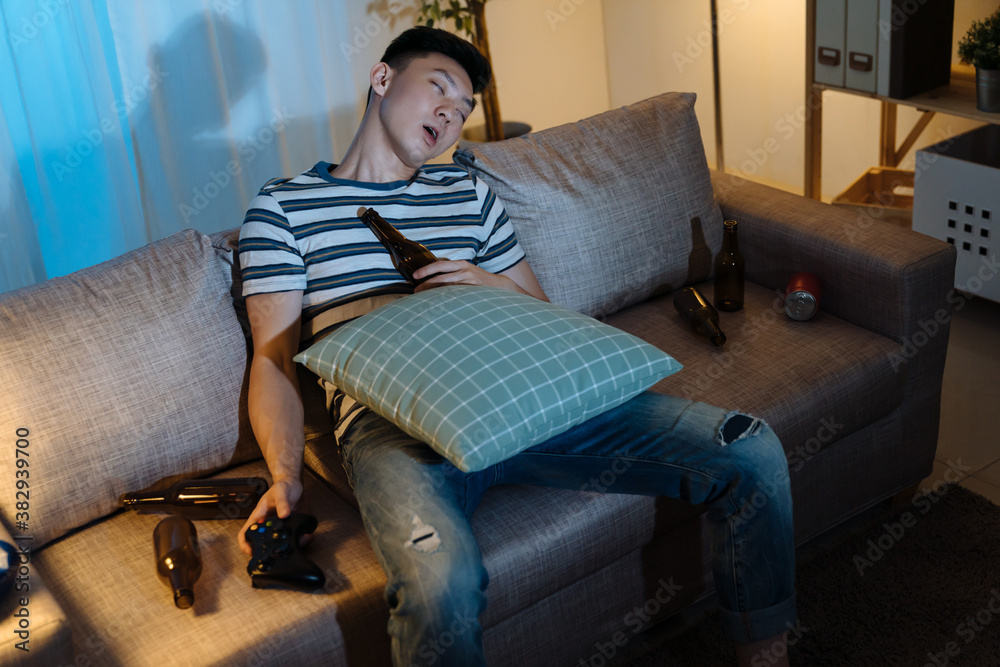 英俊懒惰的亚洲韩国男子喝完酒瓶后睡在晚上客厅的舒适沙发上