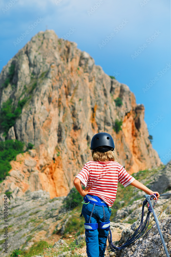 Child in safety equipment stand under mount top. Look at amazing landscape. Family travel, via ferra