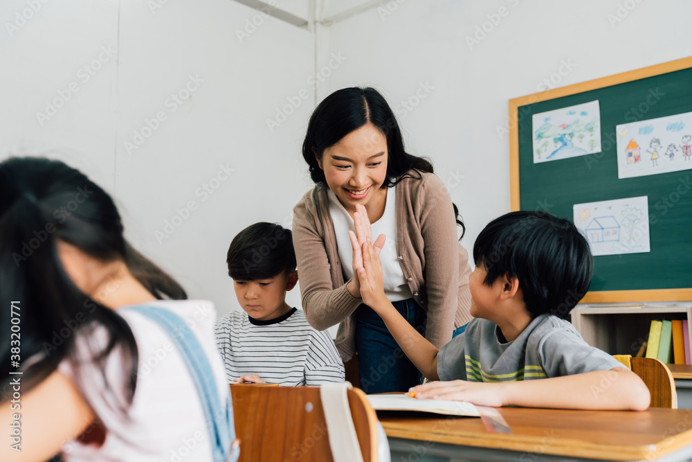 Young Asian teacher giving boy high five in school, success, achievement, happiness. Asia school boy