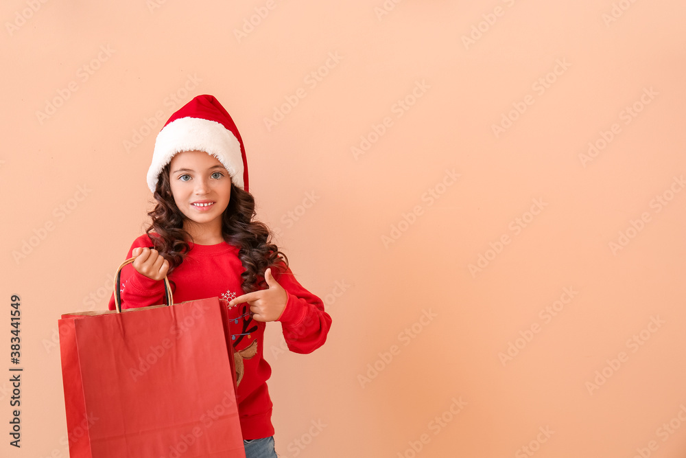 Cute little girl in Santa hat and with shopping bag on color background
