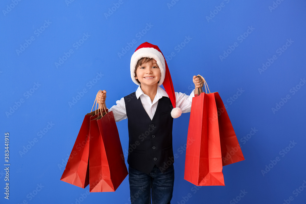 Cute little boy in Santa hat and with shopping bags on color background