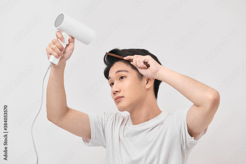 Young asian man holding hair dryer and comb creating new hairdo on white background