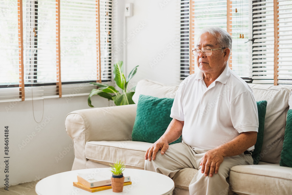 亚洲老人坐在沙发上，在家练习瑜伽和冥想，退休和健康