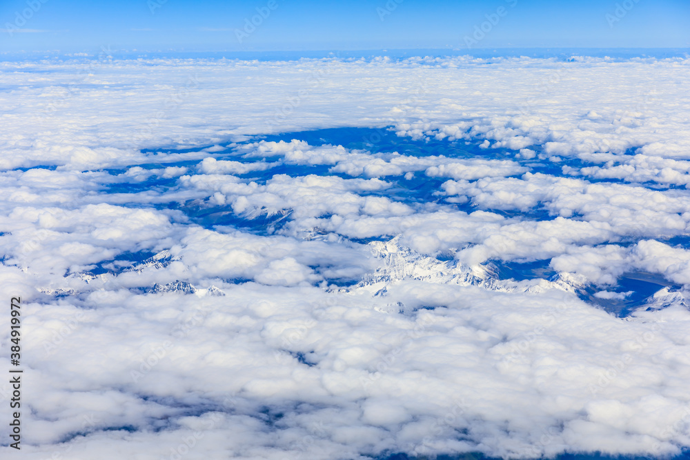 阳光明媚的日子里，云层和山峰上方的鸟瞰图。飞机上的山景。