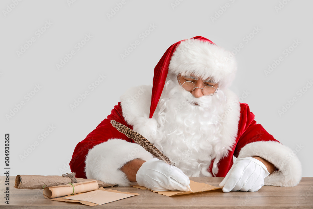 Santa Claus making wish list on light background
