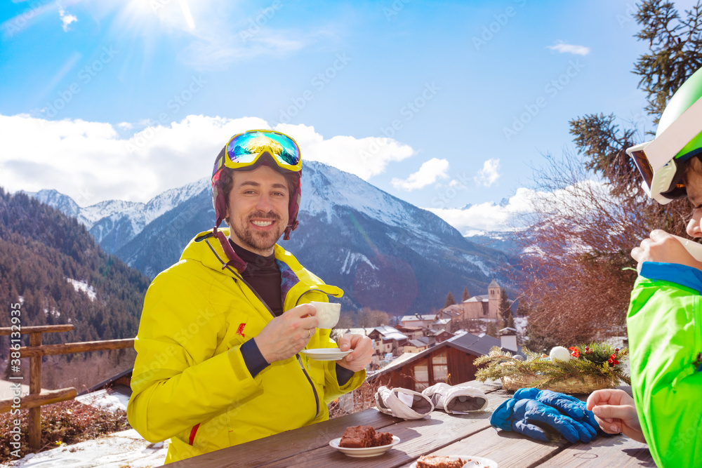 滑雪午餐后，身穿滑雪服的快乐微笑男子在山景全景咖啡馆喝茶