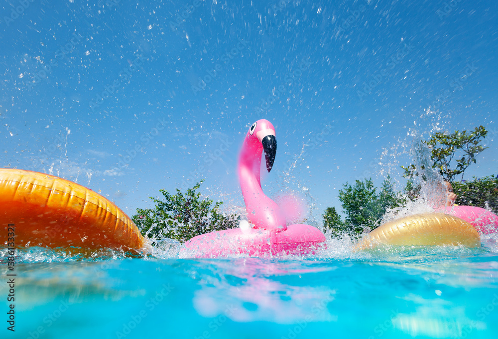 Funny action photo in the outdoor swimming pool with splashes of inflatable flamingo and doughnuts b