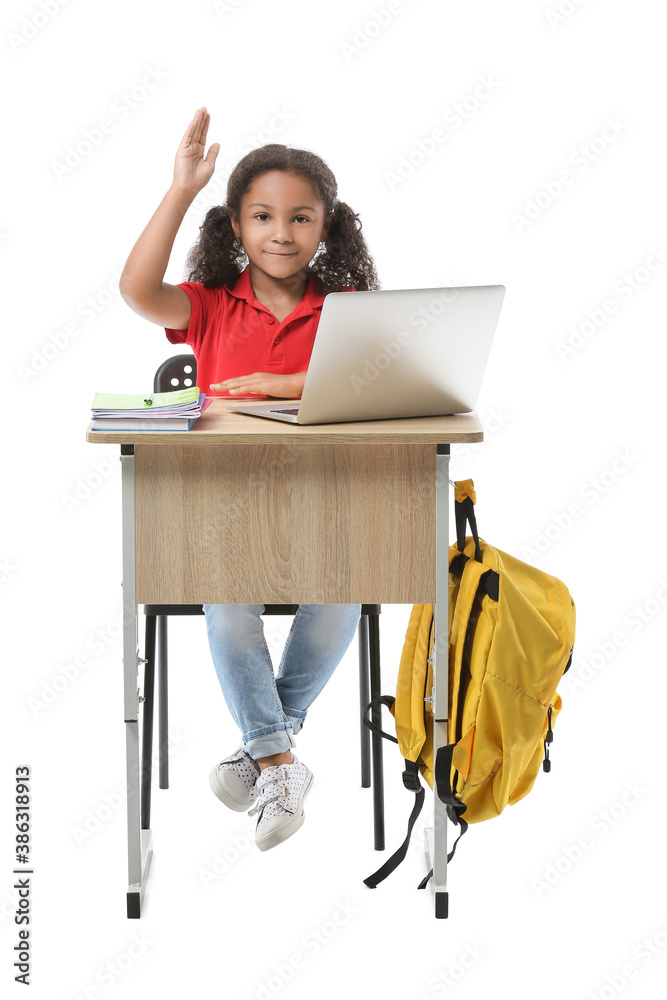 African-American schoolgirl with laptop and raised hand sitting at school desk against white backgro