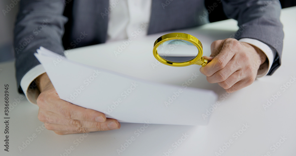 商人或审计师在办公室用放大镜检查文件。企业财务审计