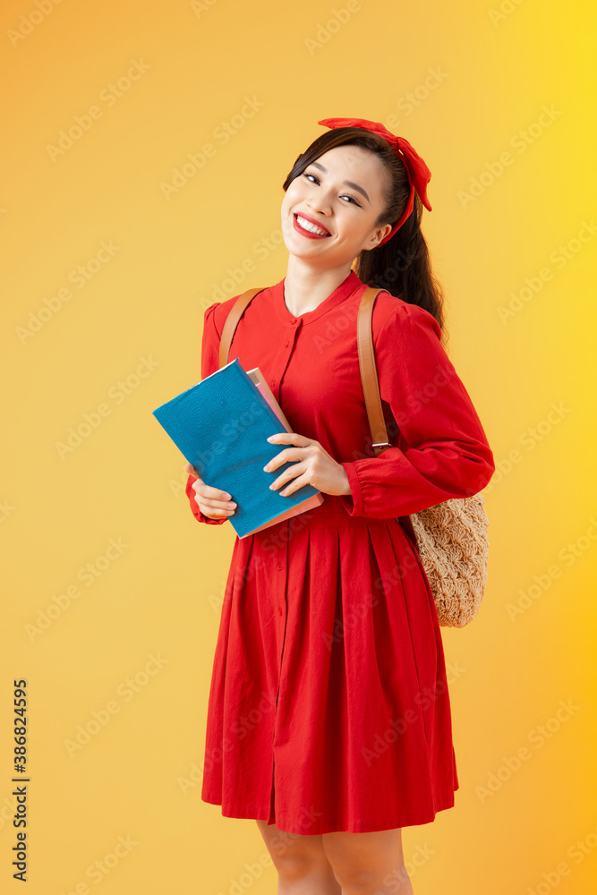 一个微笑的漂亮亚洲女孩的肖像，手里拿着书，看着橙色背景下的相机
