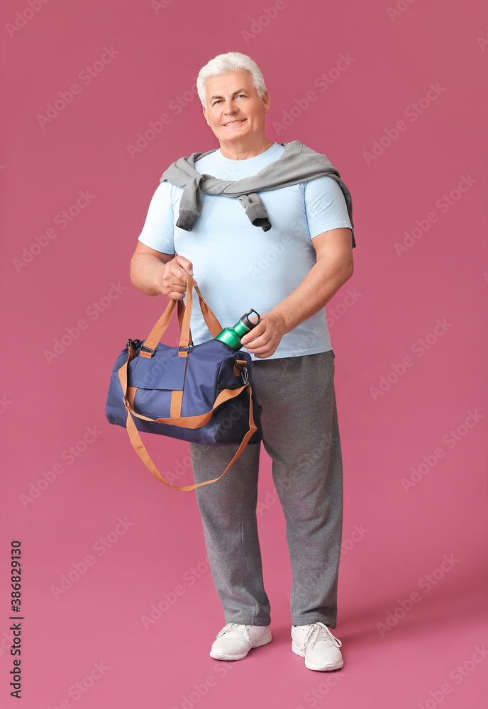 Sporty senior man with bag and bottle of water on color background