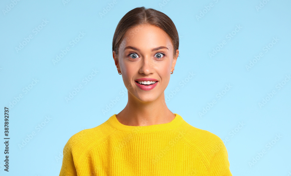 穿着蓝色背景黄色毛衣的快乐、情绪激动、惊讶的女人。