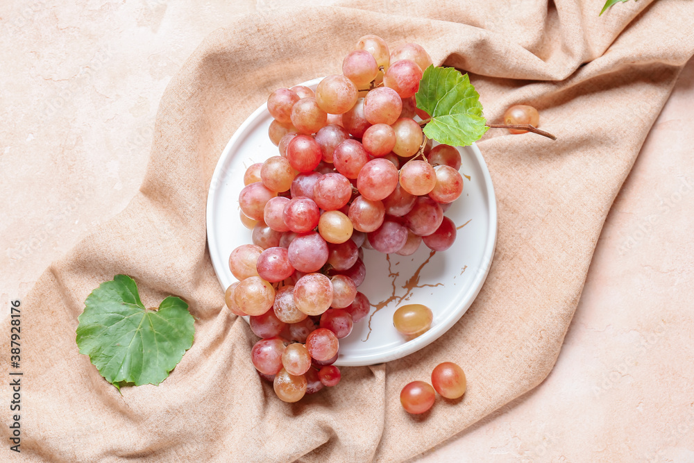 Plate with sweet ripe grapes on color background